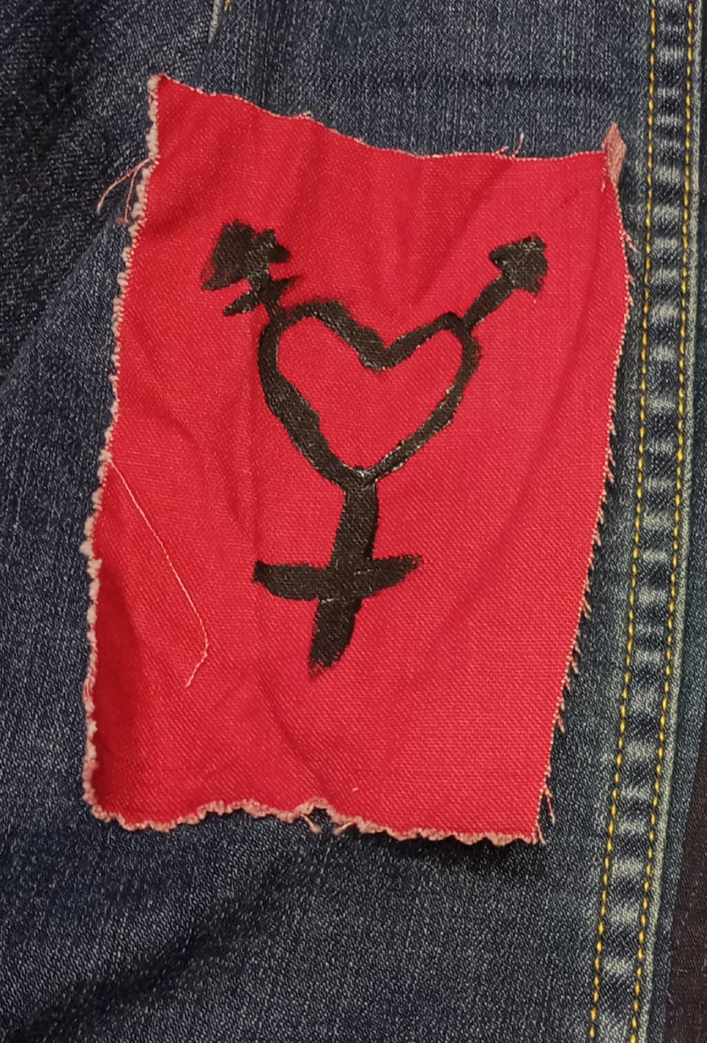 picture of a red canvas patch with a trans symbol on it. The circle of the symbol has been remplaced with a heart.